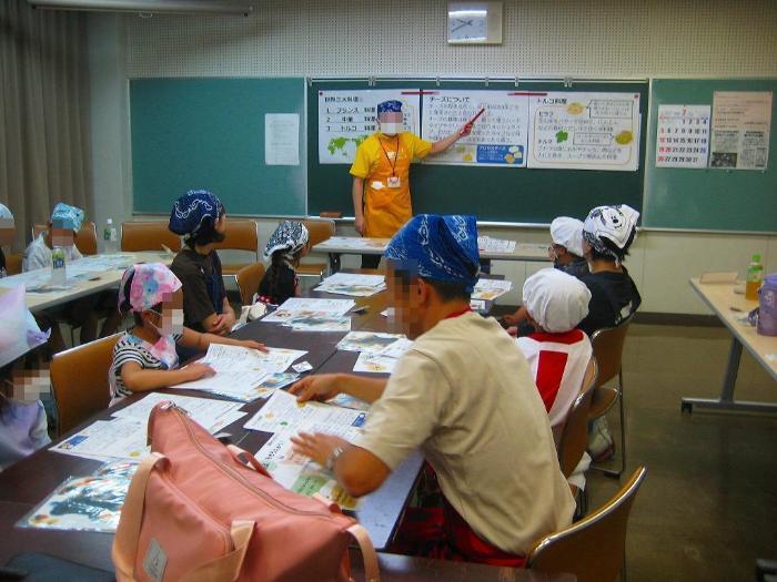 講師から世界三大料理や今回の調理手順等の説明を受ける参加者の写真