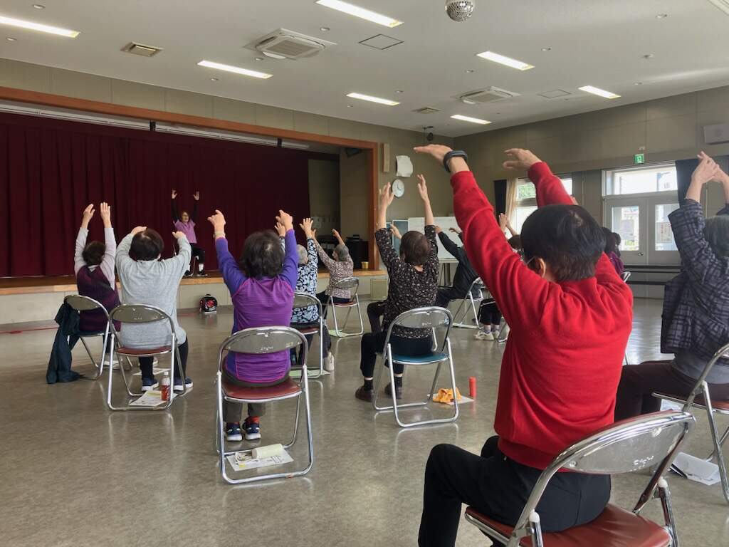 参加した高齢者の皆さんが手を挙げ、足を動かし脳活性運動運動をしている様子