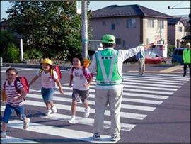 横断歩道を渡る児童らを見守る本郷自治会防犯パトロール隊員らの写真