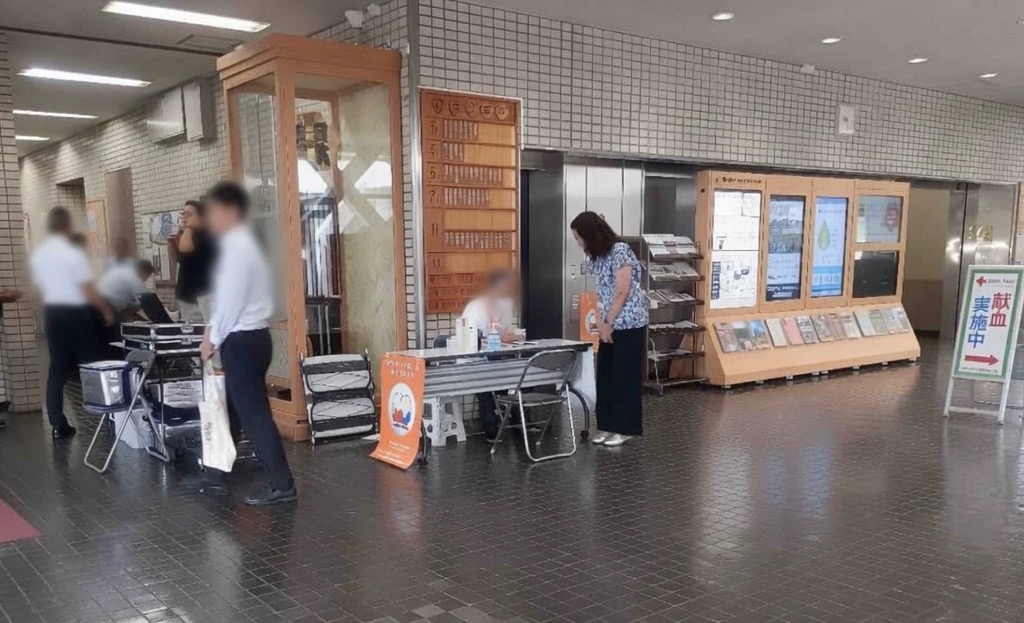 献血待合の様子。市役所エレベーターホールにて机を出して、受付をしている。人の往来が多い。