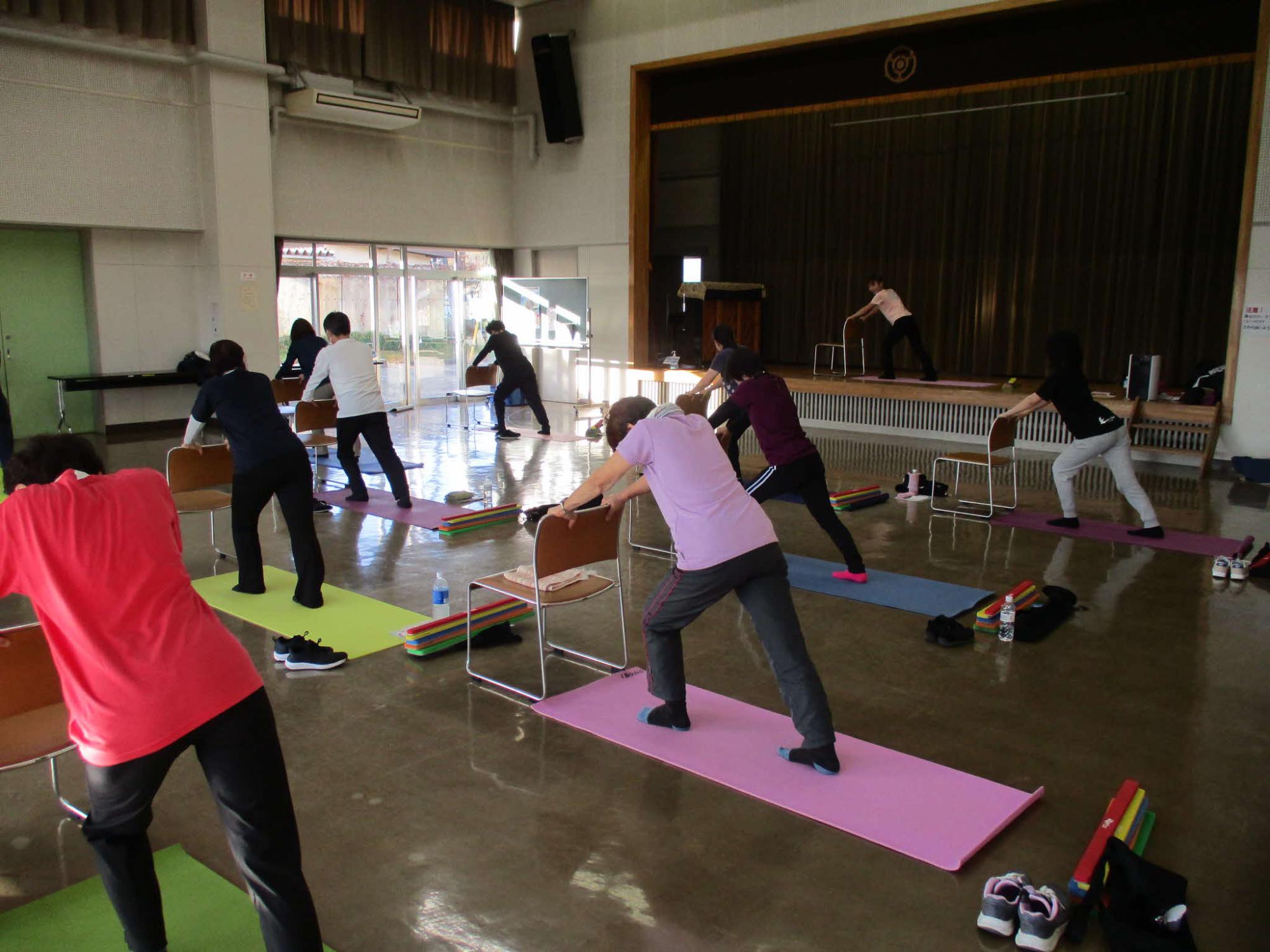 参加者が椅子の背もたれに両手をかけ、片足を後ろに伸ばしふくらはぎのストレッチをしています