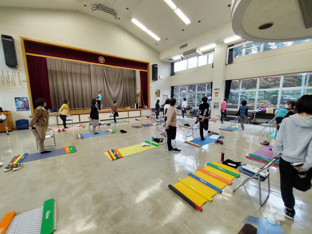 参加者が椅子の背もたれに手をかけ横向きに立ち、反対の手で後ろに上げた足のつま先を持って、もも前のストレッチをしています
