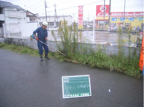 株式会社大和建設の方が、道路脇で雑草の刈払い作業をしている様子の写真
