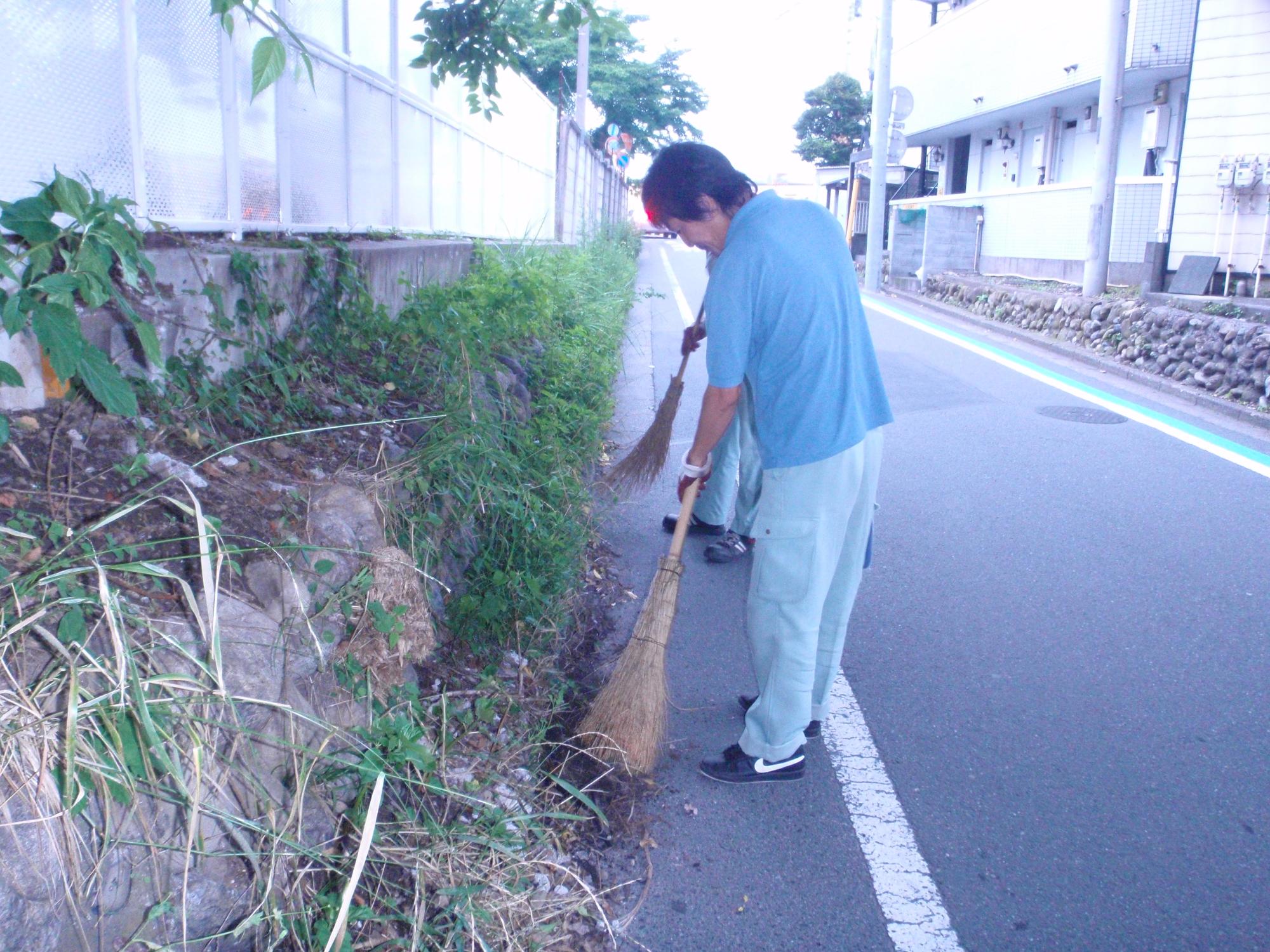 有限会社飯能清掃センターの方々が、ほうきを使って道路脇の清掃をしている様子の写真