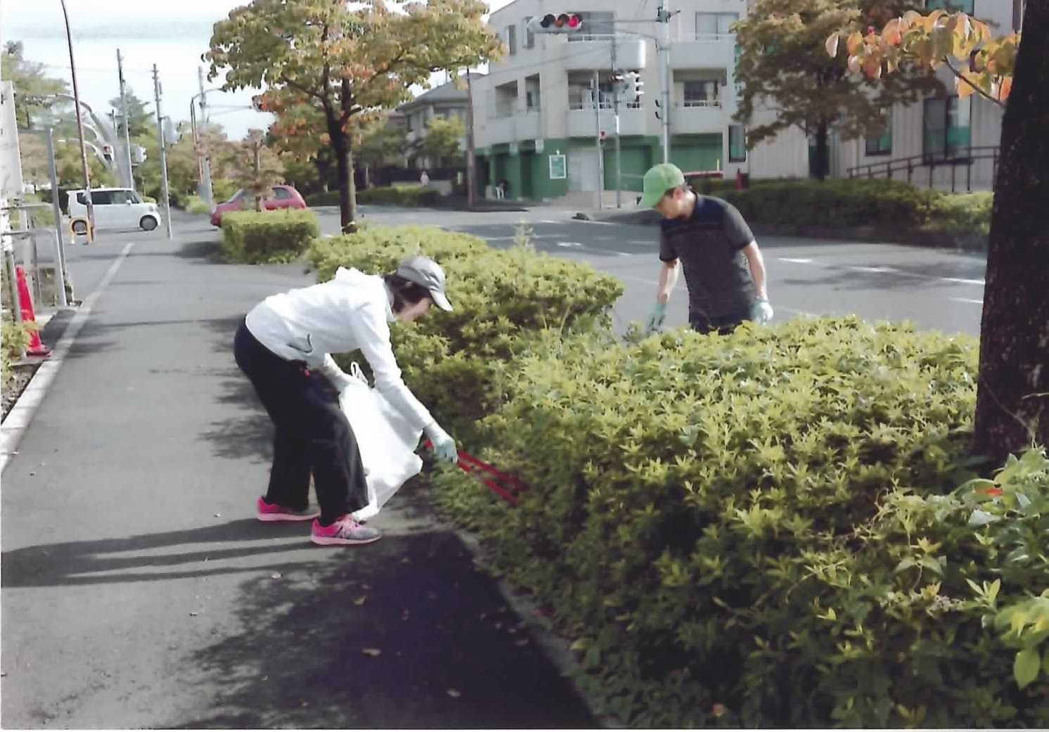 サンライズのメンバー2名が、協力して歩道の植込みの中のごみを拾っている様子の写真