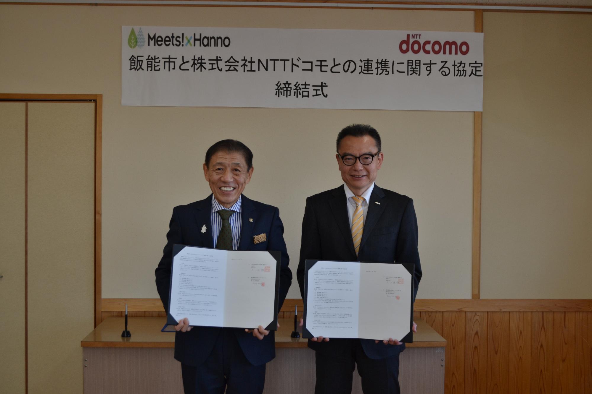 締結式で連携協定書を手に持って並んでいる市長とNTTドコモ埼玉支店長の写真