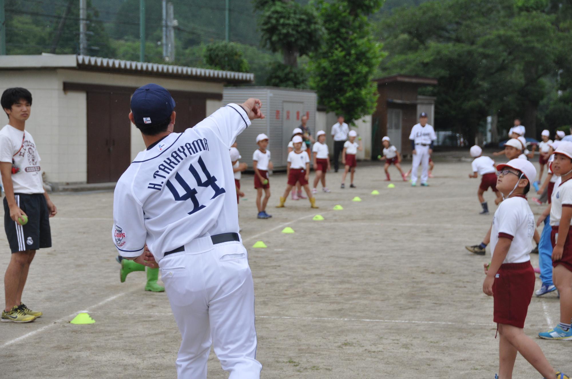 小学校の体育の授業で校庭にてベースボース型ゲームの指導をしているライオンズOBの写真