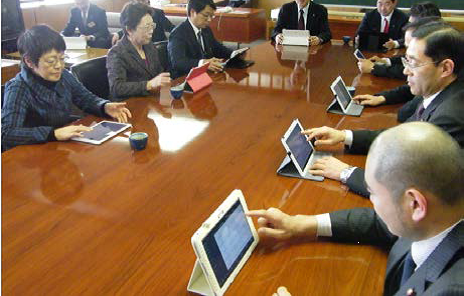 会議室で1人ずつタブレット端末を使いながら会議をしている写真