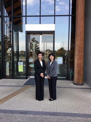 スーツを着た東京都稲城市議の女性二人が建物の前に並んで写真撮影している写真