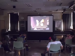 子どもたちと指導員が暗い室内で映画を観ている様子の写真