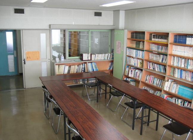 部屋の中央に長机と椅子、片側の壁一面の本棚に本が並んでいる、第2会議室の写真