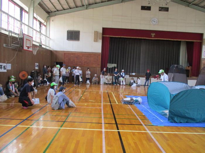 地震訓練にて体育館で避難所設営訓練をする参加者の写真