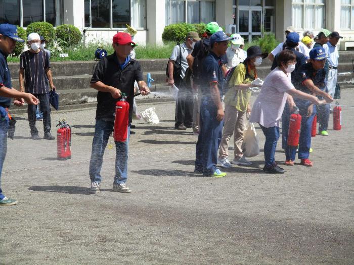 地震訓練にて校庭で水消火器による初期消火訓練をする参加者の写真