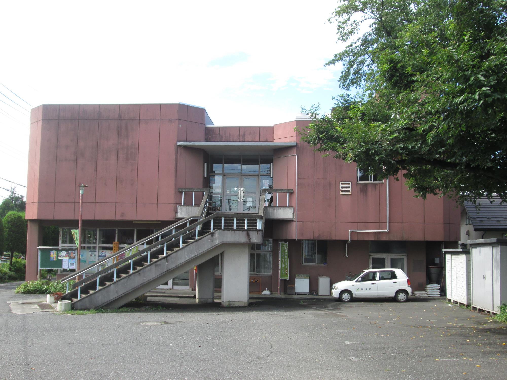 広い駐車場がある二階建ての加治地区行政センター公民館の外観の写真