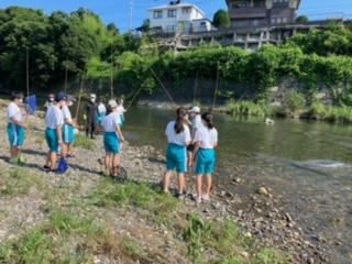 川辺で釣り竿をもって釣りをしている中学生の写真