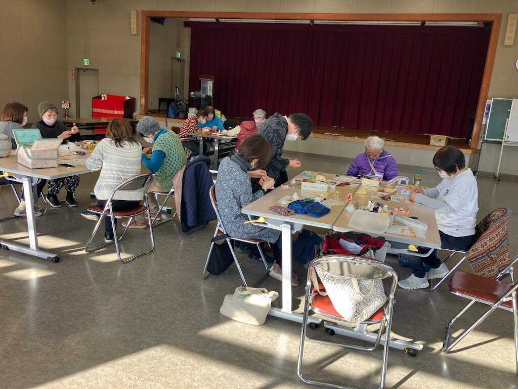 窓から午後の暖かな日差しが入る部屋で、参加した皆さんがテーブルにつき細かい作業で吊るし雛を制作している様子。