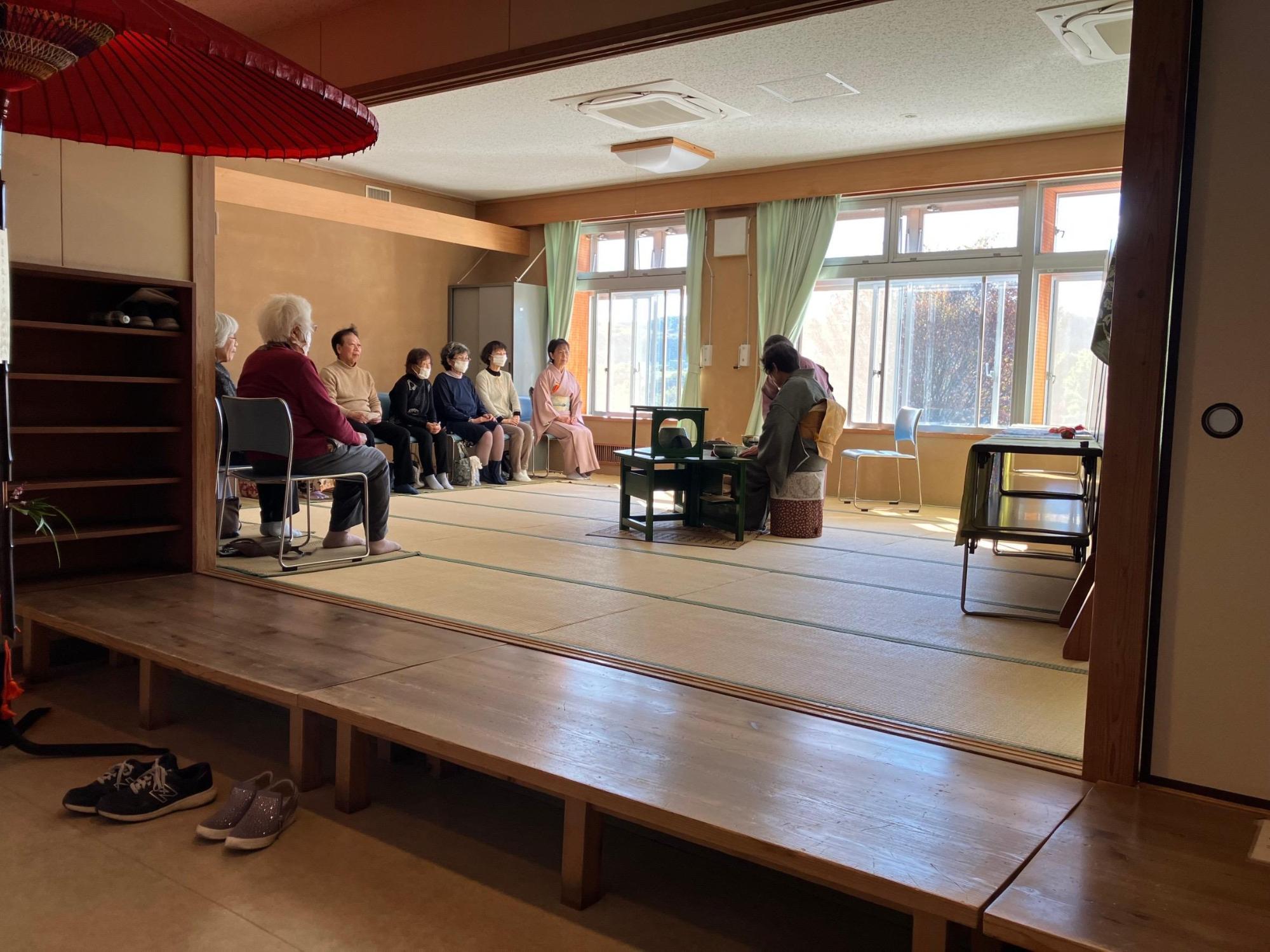 和室の入口には赤い大きな和傘。立礼式の茶席でおもてなしをしている様子。