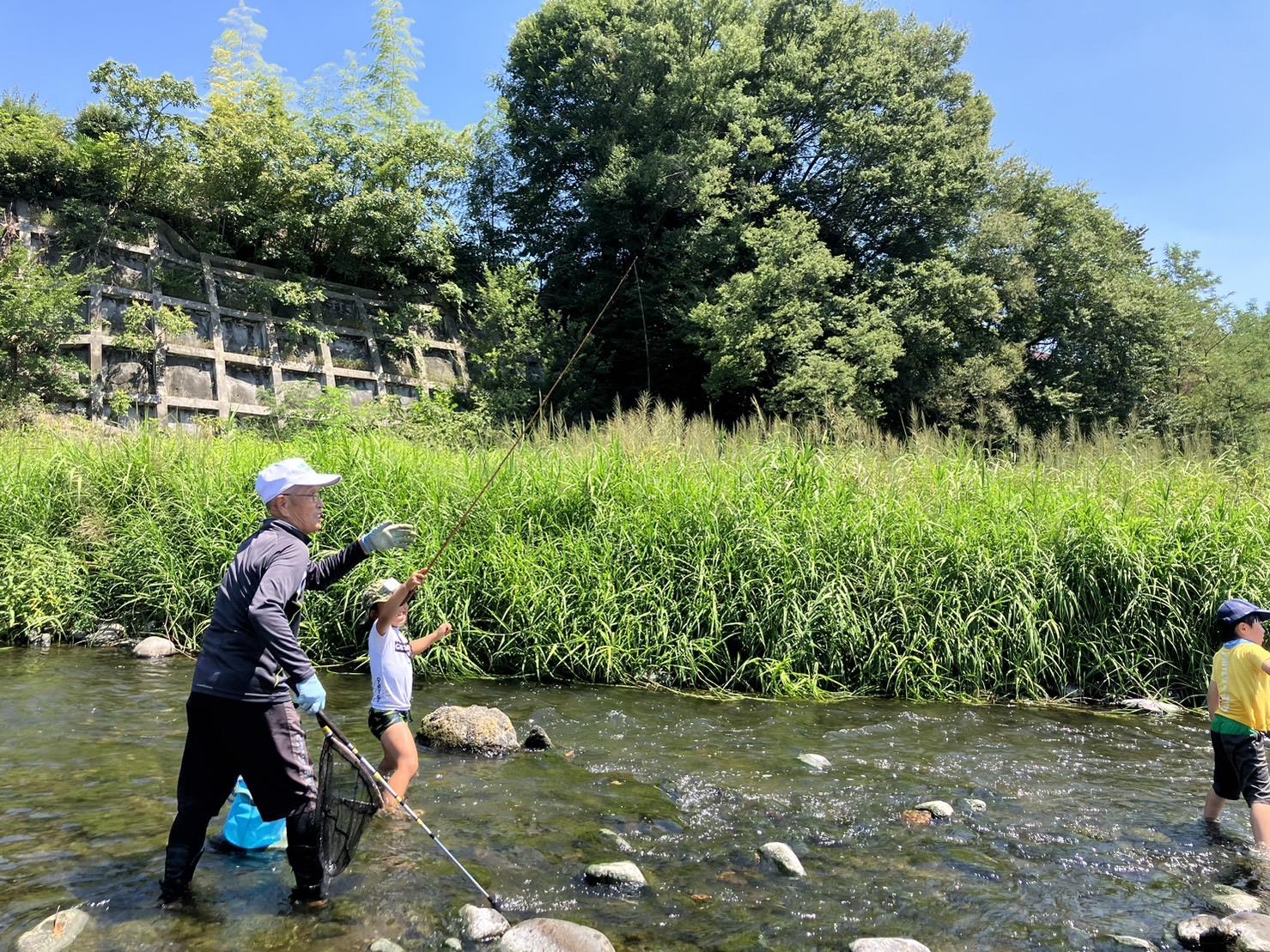 講師の近藤氏と参加者の小学生が川に入り釣りをしている様子