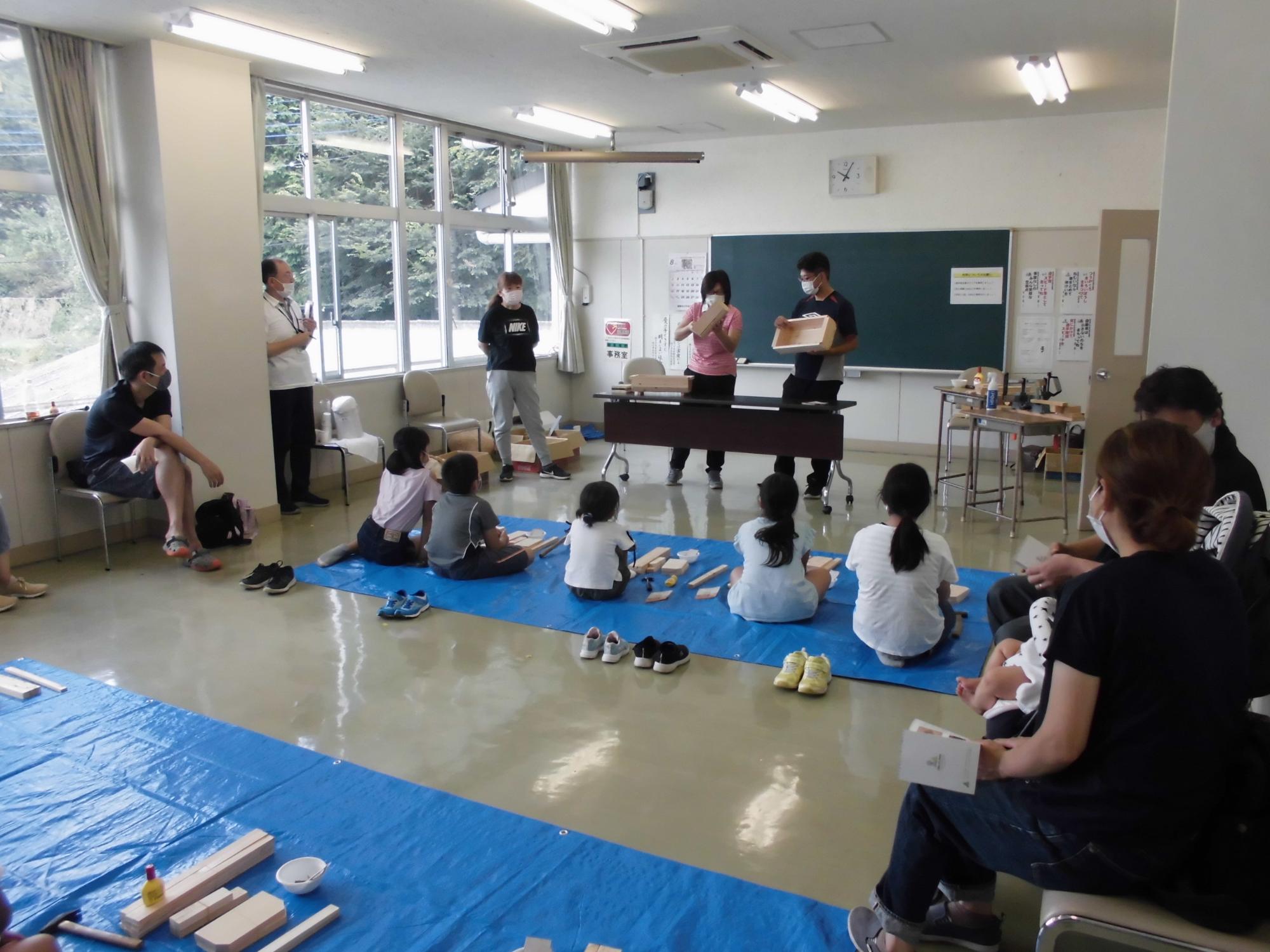 夏休み親子木工教室の参加者たちが、講師から教わっている様子の写真