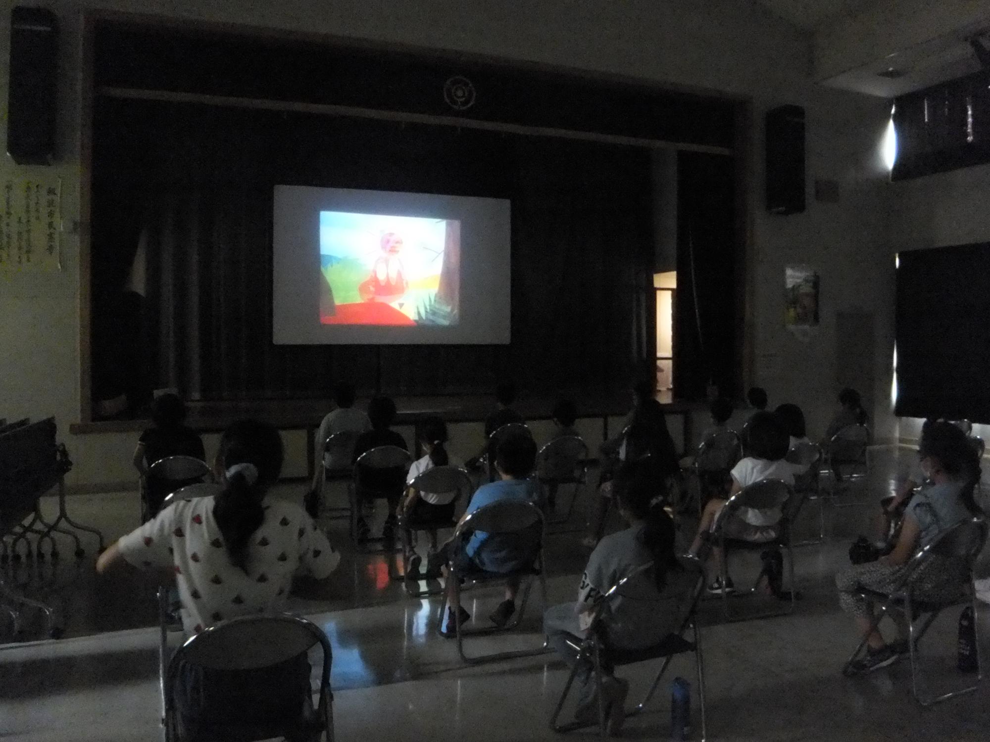 夏休み子ども映画会の参加者たちが、暗い室内で映画を観ている様子の写真