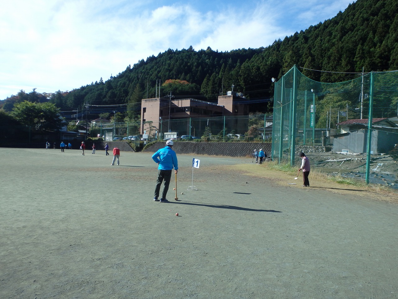 グラウンドで参加者がグラウンドゴルフ用のスティックでボールを打っている