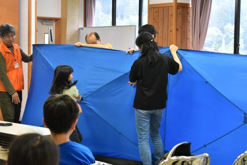 防災用パーテーションを家族で力を合わせて開いています。