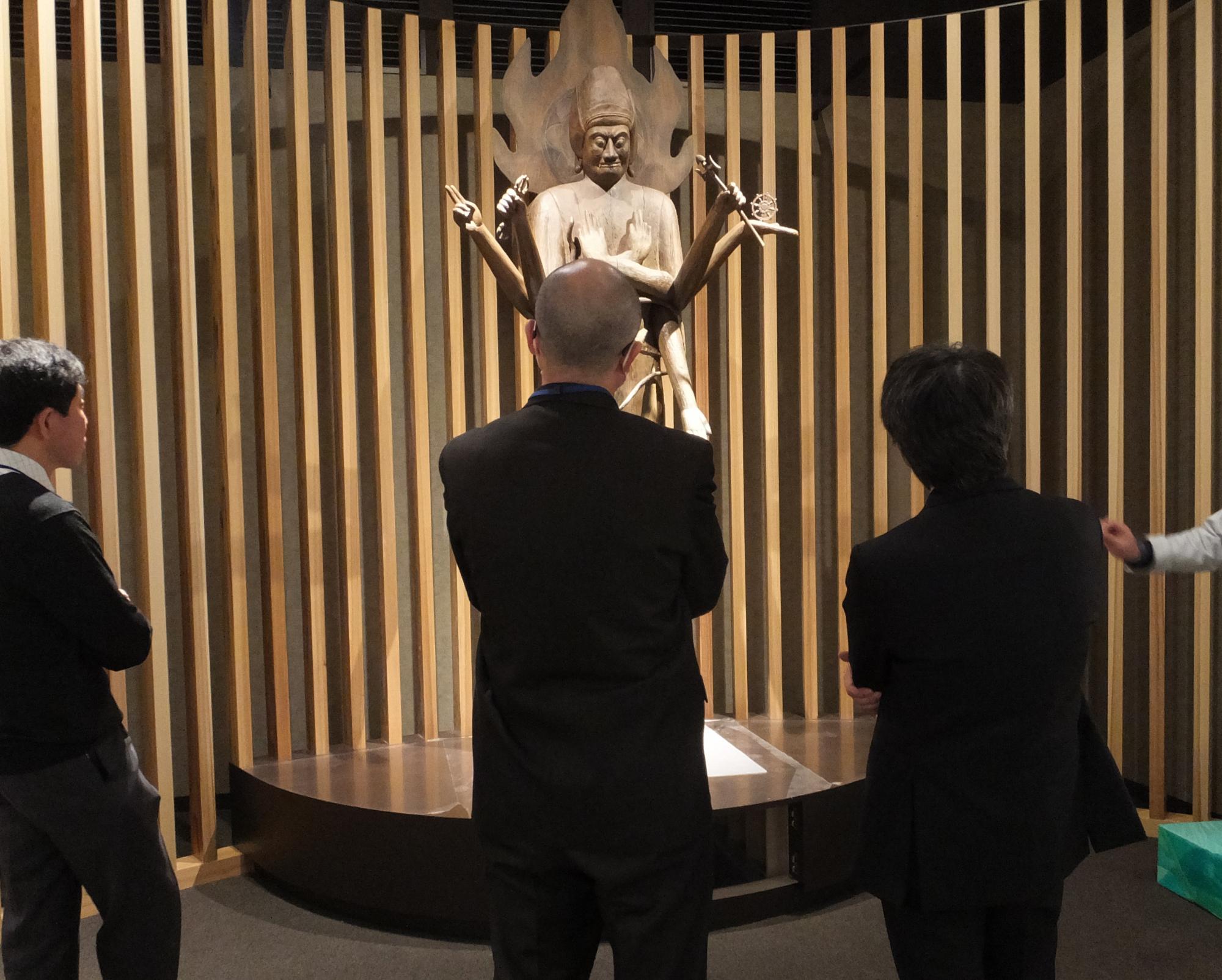 展示されている木造軍荼利明王立像を鑑賞する人たちの写真