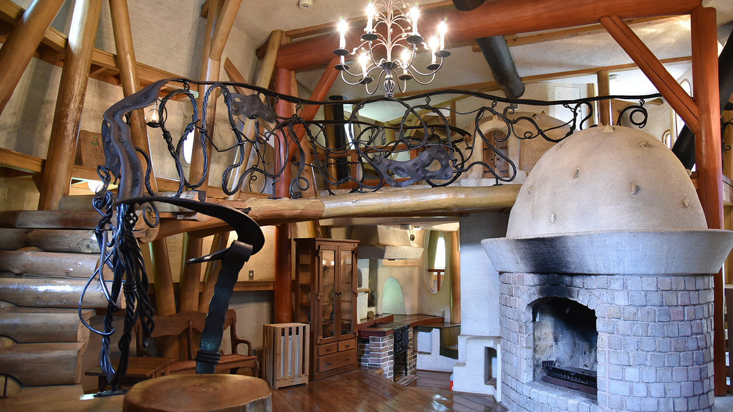 吹き抜けの天井にはシャンデリア、長椅子や飾り棚、暖炉のある木造の室内の様子
